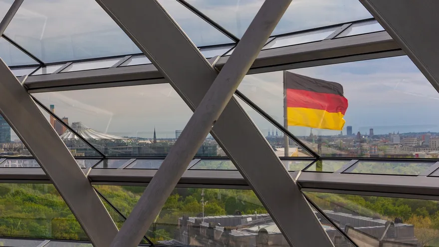 The German flag over Berlin, seen through the glass and steel lattice of the Reichstag dome, framing a study of which AI model providers German AI companies depend on.